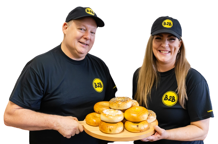 Two people holding a tray of bagels