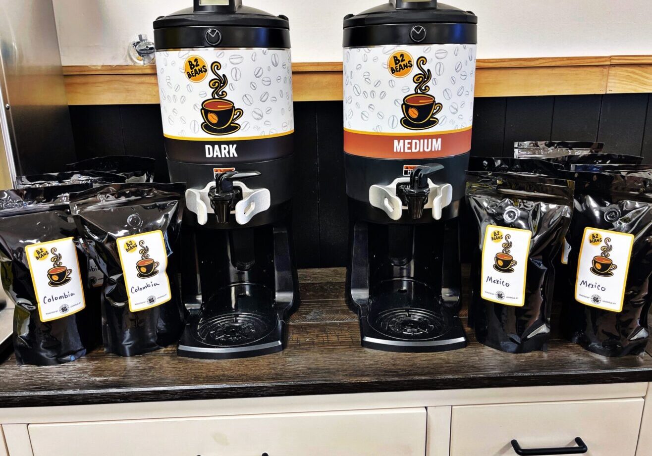 A counter with two coffee pots and many bags of coffee.